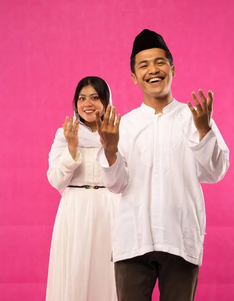 幸せなアジア系イスラム教徒のカップルの肖像画ピンクの背景に手のジェスチャーを祈るとスタンド — ストック写真