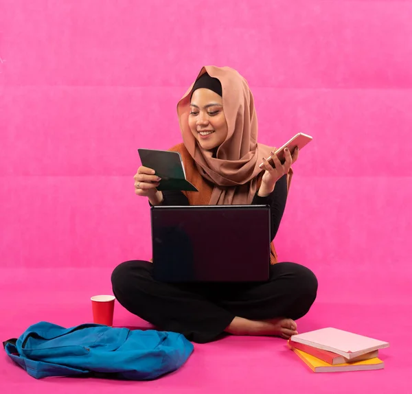 亚洲穆斯林学生坐在地板上 带着账本 用粉色背景的手机和笔记本电脑 — 图库照片