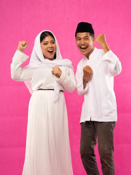 興奮したアジア系ムスリムカップルの肖像画ピンクの背景で勝利を祝うスタンド — ストック写真
