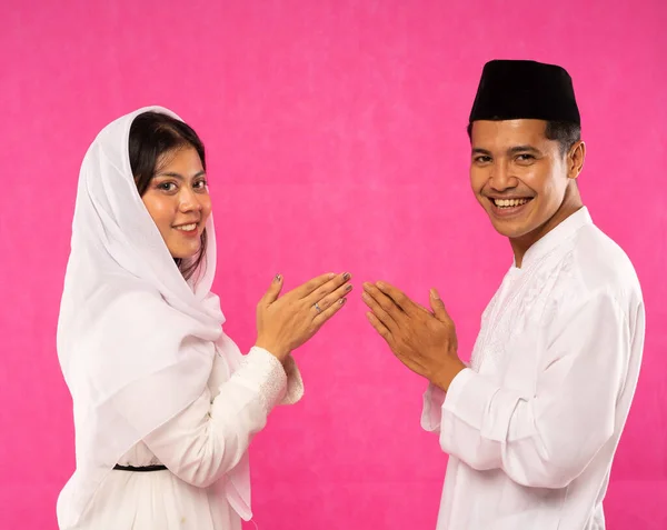 在快乐的亚洲夫妇的亲密陪伴下 他们身着粉色背景的穆斯林服装 举手投足问候 — 图库照片
