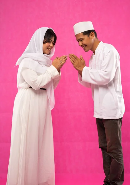 ピンクの背景をしたモスレムの服で挨拶のジェスチャーでアジアのカップルの側のビュー — ストック写真