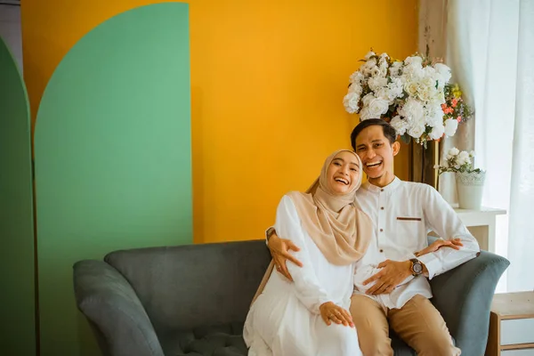 若いです結婚したイスラム教徒のカップルが喜んで楽しみを持って笑いますソファに一緒にリビングルームに座って — ストック写真