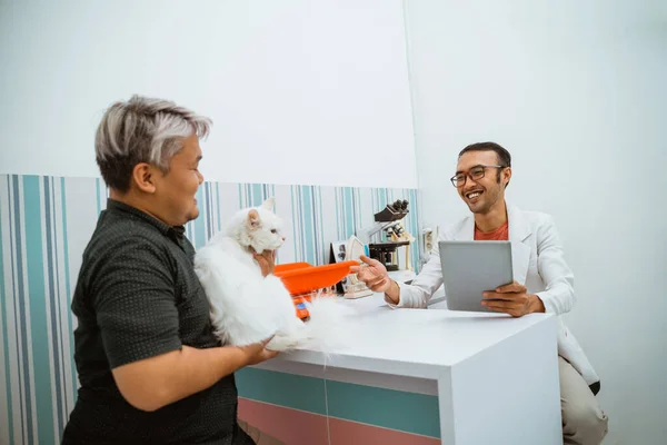 a male pet owner met the male vet at petcare bring his white cat with him for medical check up