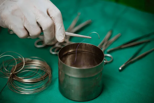 a vets hand taking surgical suture with tweezer for surgery at pets clinic