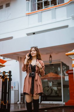 Kahverengi trençkotlu kadın gezgin telefon ediyor.