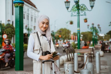 tesettürlü güzel gezgin gülümseyerek kaldırımda dururken telefonu ve pasaportu getir.