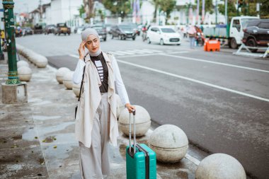 Başı ağrıyan bir kadın yolcu kaldırımda yürürken başını okşar ve bavulunu getirir.