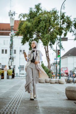 Kaldırımda yürürken telefonu tutan kolsuz ceketli Müslüman gezgin.