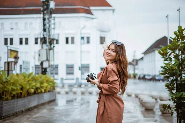 stock image beautiful traveller with long brown hair pointing on the building while holding the camera and standing at the sidewalk