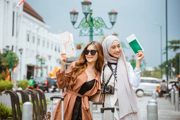 歩道に立って地図とパスポートを持ちながら抱き合っている2人の女性 — ストック写真