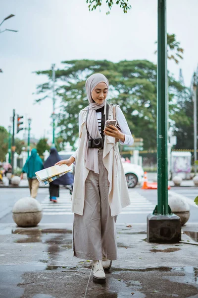 ヒジャーブ州の女性旅行者は歩道を歩きながら地図を持って携帯電話を見て — ストック写真
