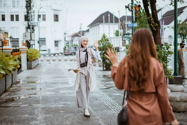 ヒジャーブのある女性旅行者が歩道を歩きながら出会った友人に手を振って — ストック写真