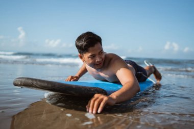 Genç erkek sörfçü sahilde kumda çalışırken sörf tahtasında kürek çekiyor.