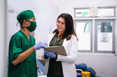 Yeşil üniformalı doktor, beyaz üniformalı doktorla kan nakli odasında sohbet ediyor.