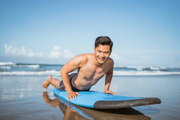 亚洲男子冲浪运动员在沙滩上的冲浪板上练习划桨后就离开了 — 图库照片
