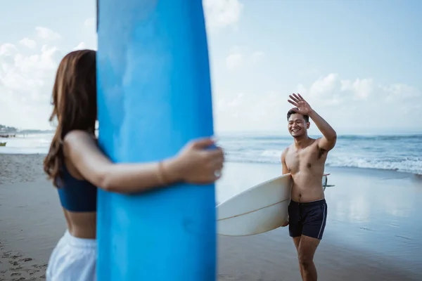 男子冲浪手在蓝天海滩背着冲浪板与女友相见 — 图库照片