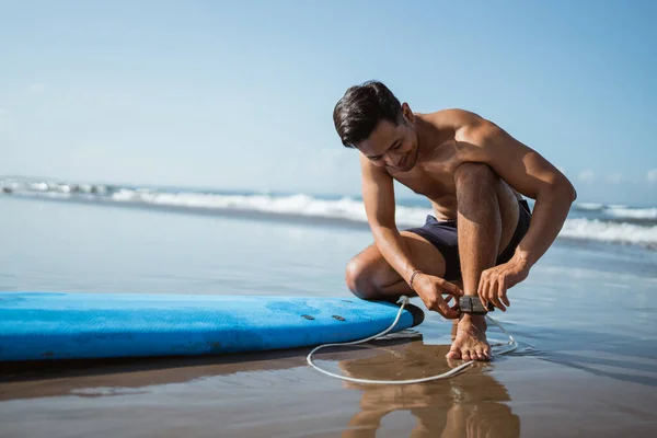 男子在海滩冲浪前系上安全带 将脚与冲浪板相连 — 图库照片