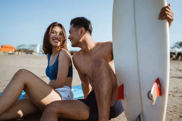 情侣们喜欢坐着聊天 一边在沙滩上拿冲浪板 — 图库照片