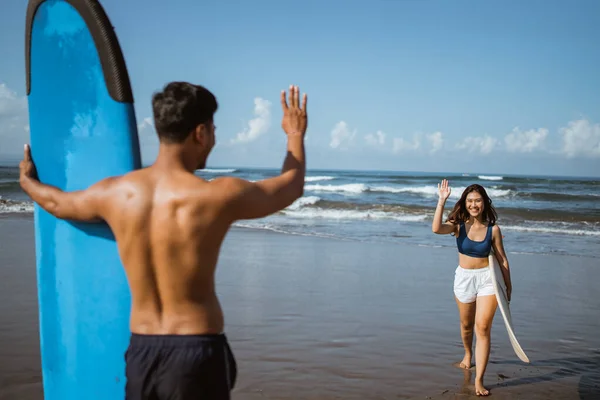 女冲浪者在练习完冲浪板后 和一个在海滩上冲浪的男人打招呼 — 图库照片