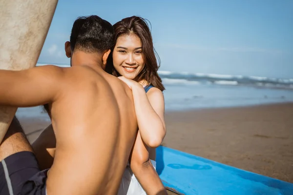 在海滩沙滩上坐在冲浪板边拥抱伴侣的浪漫美丽的女人 — 图库照片