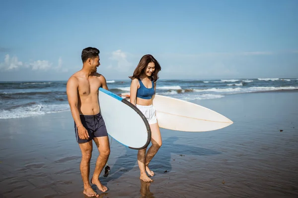 穿着泳衣的快乐夫妇在训练后背着冲浪板在海滩上散步和开玩笑 — 图库照片