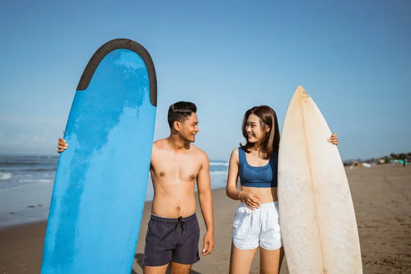 在海滩边聊天边拿冲浪板的亚洲年轻夫妇的画像 — 图库照片