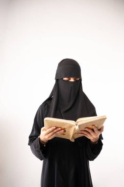 Müslüman kadın siyah başörtüsü ya da niqab takıyor ve uzun siyah elbise Al Quran 'ı okuyor.