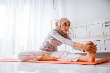 Asyalı Müslüman kadın eğitmen yoga pilatesi giyip turuncu yatakta poz veriyor.