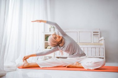 Asyalı Müslüman kadın eğitmen tesettür takmış yoga pilates yaparken yukarı bakıyor turuncu yatakta özel ders veriyor.