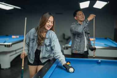 Kadın bilardo oyuncusu bilardo toplarını yerleştirirken erkek oyuncu da maçtan önce tebeşiri atıyor.