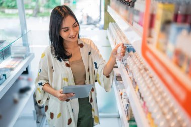Güzel bir dükkan sahibi dijital masayı kullanarak raftaki sıvı stoku kontrol ediyor.