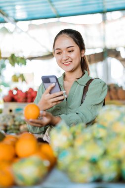 Kadın müşteri telefonla Mandarin meyvesinin fotoğrafını çekerken gülümsüyor.