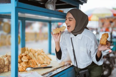 Başörtüsü takan güzel bir kız yol kenarında el arabası olan çeşitli kızarmış yiyecekler satıyor.