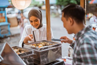 Adam yol kenarında el arabası olan çeşitli hamur köfteleri satıyor.