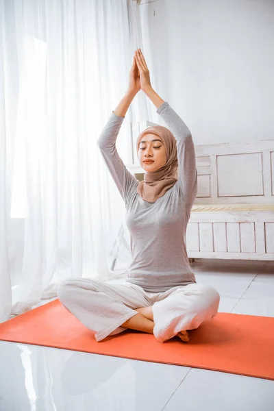 健康的穆斯林妇女 头戴头巾 做瑜伽枕头 在橙色床垫上沉思 眼睛闭着荷花 在房间里摆姿势 — 图库照片