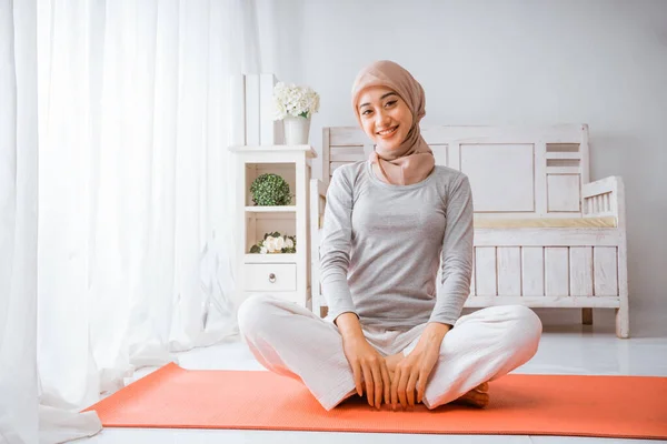 健康なイスラム教徒女性身に着けていますTシャツ白いパンツヒジャーブ行いますヨガピラティス笑顔でオレンジマットレスで部屋 — ストック写真