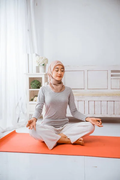 健康的穆斯林妇女 头戴头巾 做瑜伽枕头 在橙色床垫上沉思 眼睛闭着荷花 在房间里摆姿势 — 图库照片