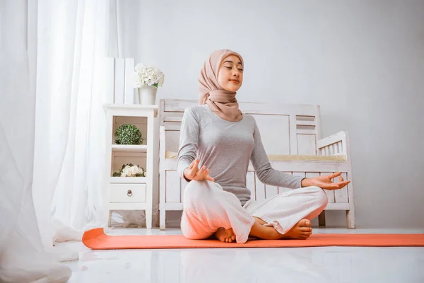 健康的穆斯林妇女 头戴头巾 做瑜伽枕头 在橙色床垫上的房间里沉思 眼睛闭着 侧卧着 房间里摆着荷花 — 图库照片