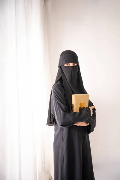 身穿黑色头巾或Niqab和黑色长裙的穆斯林妇女站在一个房间里 手里拿着一只四头蛇 一边看一边看 — 图库照片