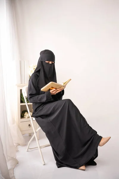 身穿黑色头巾或Niqab的穆斯林妇女 穿着黑色长裙坐在椅子上看书或诵经 — 图库照片