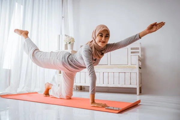 在做瑜伽或普拉提运动前 穿着头巾T恤衫的穆斯林女性微笑着躺在房间的床垫上 — 图库照片