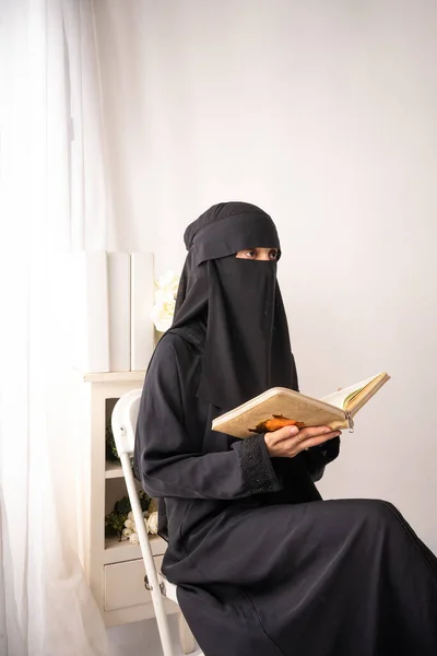 身穿黑色头巾或Niqab和黑色长裙的穆斯林妇女坐在椅子上看书或看前面的书刊 — 图库照片