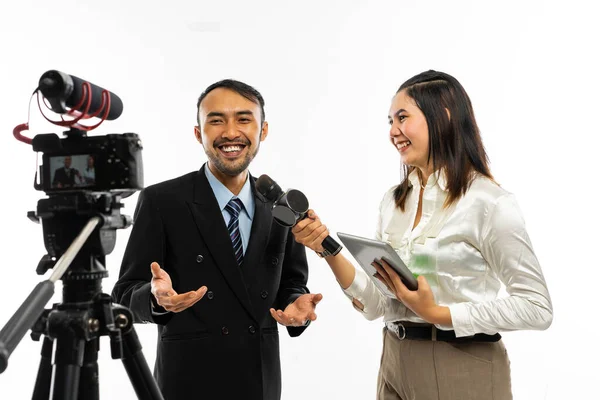 マイクを使って美しい女性ジャーナリストのインタビューを受けながらカメラと話をしている黒いスーツの大人の男性 — ストック写真