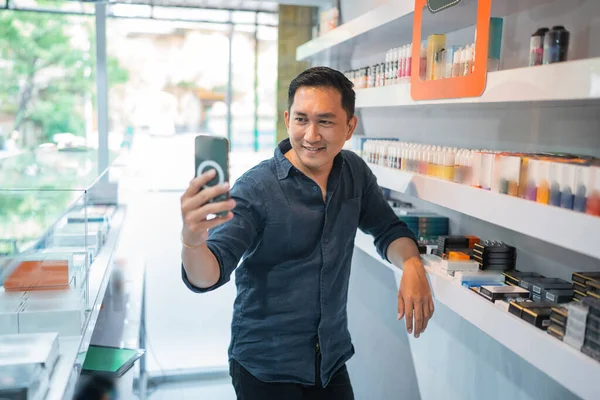 男蒸汽销售员站在商店货架旁边用手机拍自拍照 — 图库照片