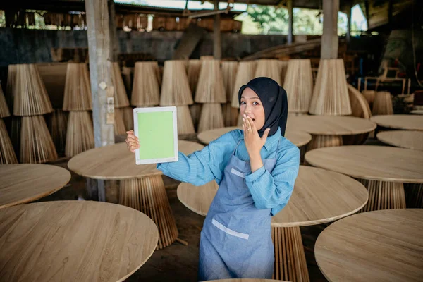 アジアのベールビジネス女性は 木製の工芸品店で手のひらで彼女の口をカバーしながら タブレット画面を示しています — ストック写真