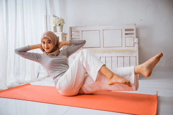 アジアのイスラム教徒女性インストラクター身に着けているヒジャーブヨガピラティスポーズチュートリアル上のオレンジマットレスで部屋 — ストック写真