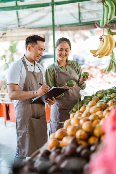 一对亚洲水果销售商检查水果并在剪贴板上书写 — 图库照片
