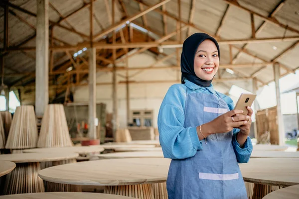 Stock image smiling veiled businesswoman holding a cell phone while standing in a woodcraft shop