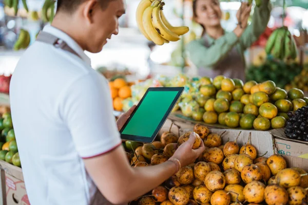 男性员工手握绿色屏幕数码平板电脑 同时在果品店观看充满激情的水果 — 图库照片