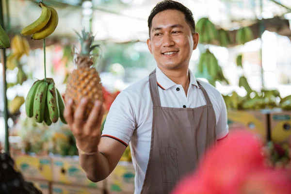 Όμορφος Πωλητής Φρούτων Χαμογελώντας Κοιτάζοντας Τον Ανανά Στο Χέρι Του — Φωτογραφία Αρχείου